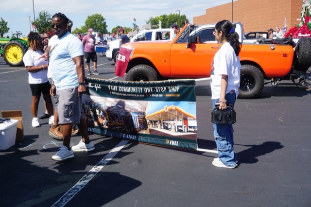 Two team members holding the Kumbha-Yah banner open in the staging lot, beside a vintage orange truck