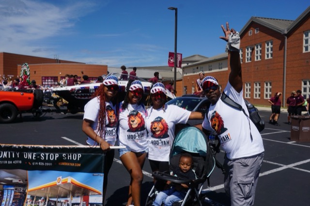 A team member with one arm raised in celebration, the rest of the group and a baby in a stroller beside him