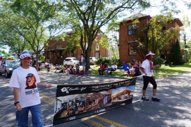 Carrying the Kumbha-Yah banner along the parade route, spectators watching from the shade