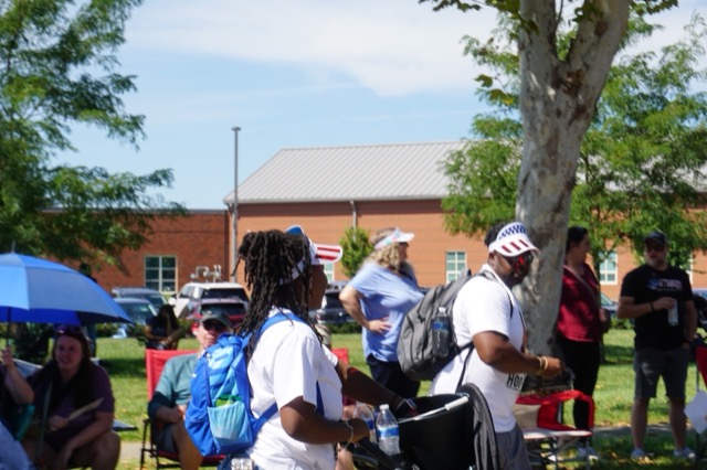 Team members stopping to greet neighbours seated under umbrellas along the route