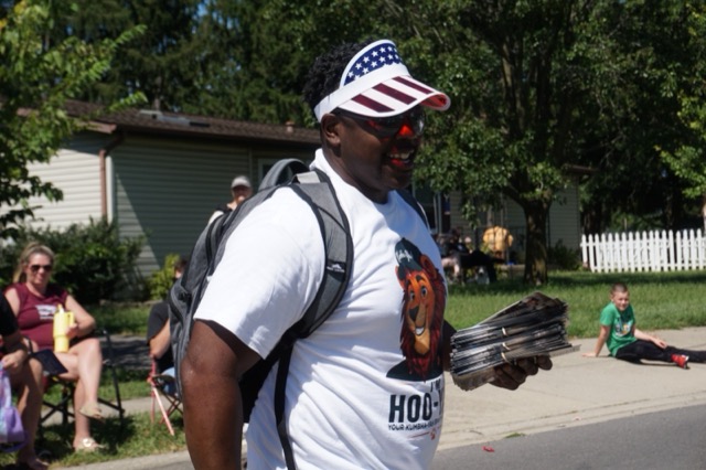 A team member in a Hoo-Yah! shirt handing out flyers to families sitting on the grass